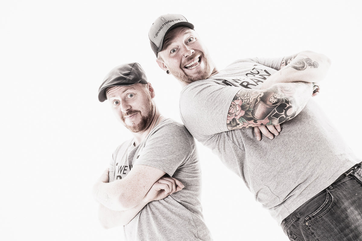 Tom und Olly von gezeichneteslicht lachend Rücken an Rücken vor weißem Hintergrund